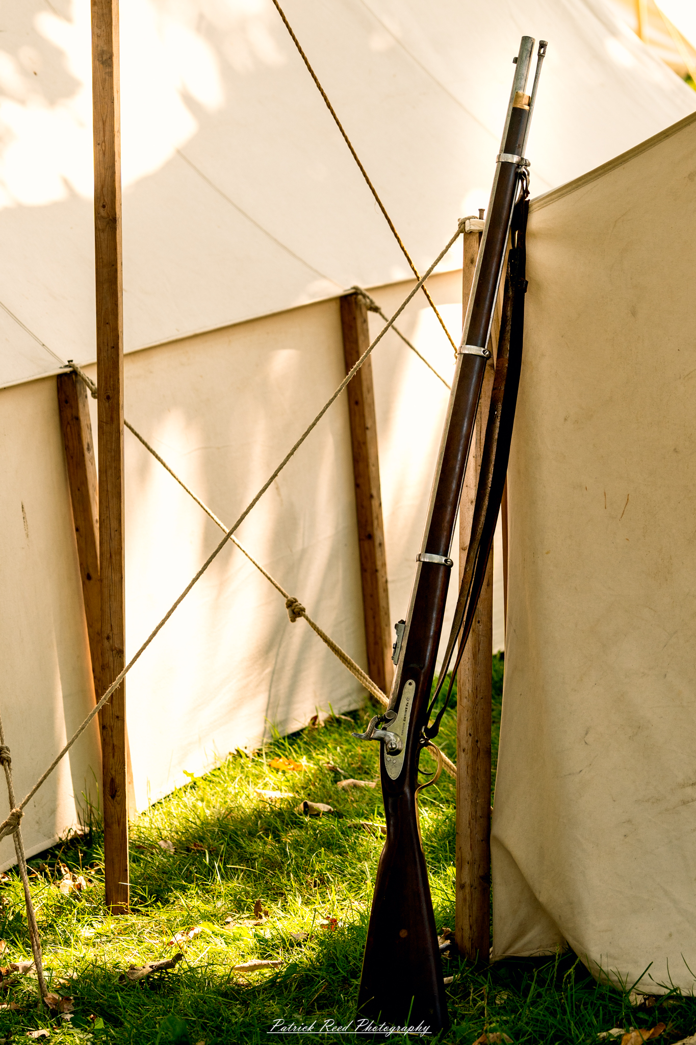 A rifle leaning against a tent, positioned casually as if momentarily set aside. The scene conveys a sense of military life, with the tent's fabric fluttering slightly in the breeze, suggesting the presence of soldiers nearby and the everyday realities of camp life.